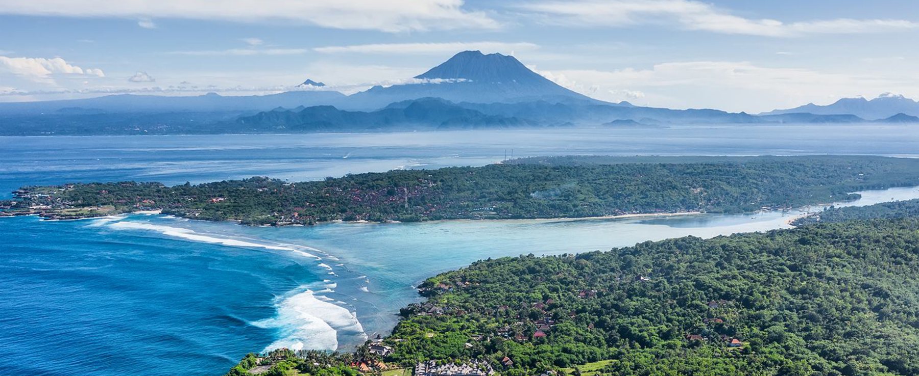 Aerial view of the Bali coastline with the volcanoes rising beyond